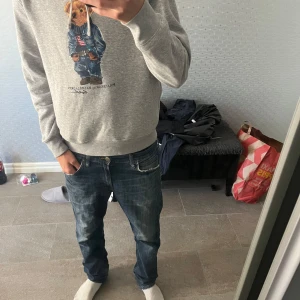 Grå hoodie Polo Bear från Ralph Lauren - Säljer en grå hoodie från Polo Ralph Lauren med ikoniska Polo Bear-trycket på bröstet. Tröjan har huva med snörning, ribbade muddar och är tillverkad i mjuk bomullsmix. Perfekt för dig som gillar något bekvämt men ändå snyggt. Inga defekter och priset är inte hugget i sten! Har ni frågor eller funderingar är det bara att höra av dig! 😁