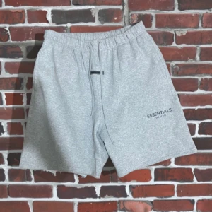 Grå shorts Essentials Fear of God XL - Snygga grå shorts från Essentials Fear of God i mjuk bomull. De har elastisk midja med snörning och logga tryckt på benet. Perfekta för chill dagar eller när du vill ha en clean streetwear-look.