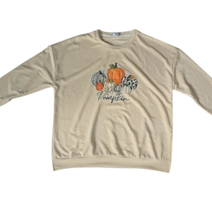 Beige sweatshirt med pumpatryck XL - Beige sweatshirt i storlek XL med färgglatt pumpatryck och texten 'Hey Pumpkin' på bröstet. Tröjan är tillverkad i 100% polyester och har en avslappnad passform med långa ärmar. Perfekt för höstmys och att sticka ut lite extra.