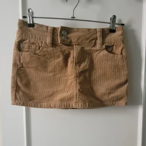 Beige manchesterkjol från H&M Divided - Beige kortkjol i manchester från H&M Divided. Kjolen har klassisk femficksdesign, två knappar och dragkedja framtill. 