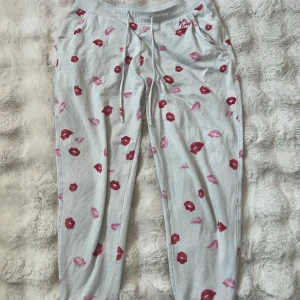 Grå mjukisbyxor med läppar från hollister  - Vita mjukisbyxor med drag i midjan och ett lekfullt mönster av röda och rosa läppar. Byxorna har resår i midjan och sidofickor, perfekta för en avslappnad och samtidigt snygg stil. 
