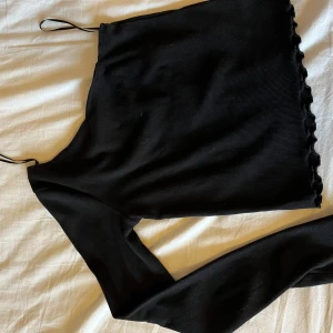 Svart oneshoulder topp med volangkant - GE PRISFÖRSLAG! Säljer en svart ribbad oneshoulder topp från Gina tricot med smala axelband på ena sidan och lång ärm på andra. Toppen har volangkant nertill och är i stretchigt material. Har aldrig använt denna då jag inte tycker den passar mig. DM om du vill ha bättre bilder!!🥰