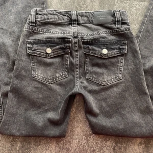 Grå jeansbyxor från Gina Tricot - Säljer ett par grå jeans från Gina med klassisk femficksdesign och raka ben. Byxorna har silverfärgade knappar och detaljer samt normal passform. Perfekta till vardags för en avslappnad stil.