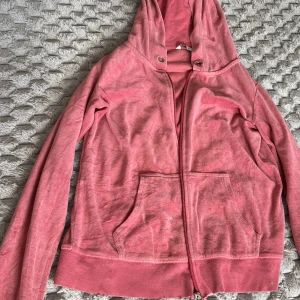 Rosa hoodie med dragkedja - Mysig rosa hoodie med dragkedja och huva. Tröjan har långa ärmar, två fickor framtill och ribbade muddar vid ärmslut och nederkant. Perfekt för en avslappnad stil eller som ett extra lager under kyliga dagar.