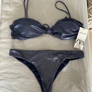 Mörkblå bikini från Zara - Snygg mörkblå bikini från Zara med glansig finish. Överdelen har smala axelband och knytdetalj framtill. Aldrig använd med prislapp kvar, men liten defekt på baksidan av underdel (se bild 3). Det går att köpa bara övderdelen/ underdelen om det skulle önskas 😊😊