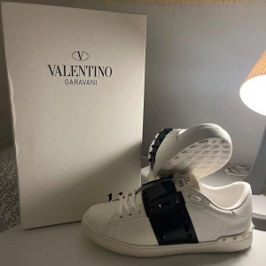 “Valentino’s Open – Stilren design med lyxig känsla” - Valentino’s Open-sneakern kombinerar italiensk elegans med en avslappnat lyxig stil. Tillverkad i premium vitt läder med den karakteristiska svarta remmen och subtila nitar, skapar den en sofistikerad kontrast som drar blickarna till sig. Den bekväma passformen, det klassiska snittet och den unika suldesignen gör den till ett självklart val – oavsett om du klär dig upp eller ner. Ett tidlöst statement från Valentino som aldrig kompromissar med stil.