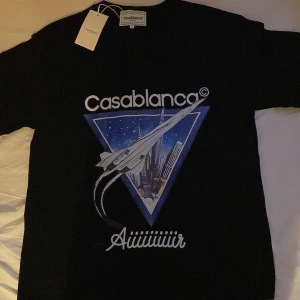 Svart t-shirt från Casablanca. - Cool svart t-shirt från Casablanca med stort tryck av ett Concorde-plan och stadssilhuett på framsidan. T-shirten har rund hals och korta ärmar. Perfekt för dig som gillar unika prints och streetwear. Den är inte använd nån gång och är helt ny. Perfekt inför sommaren