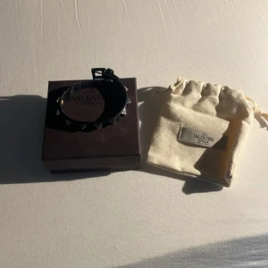 Svart armband med nitar från Valentino - Säljer ett svart armband från Valentino med silvriga nitar. Kommer i original ask och tygpåse med Valentino-logga. Perfekt accessoar för att ge din outfit en edgy touch.