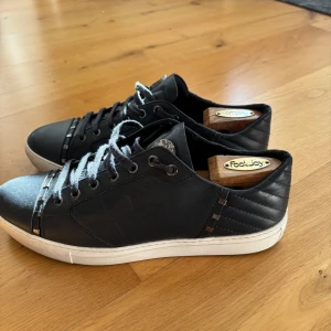 Verasace Collection skor - Säljer ett par mörkblå sneakers från Versace med snygga silverdetaljer på sidan och fram på skon. Knappt använda så i väldigt bra skick