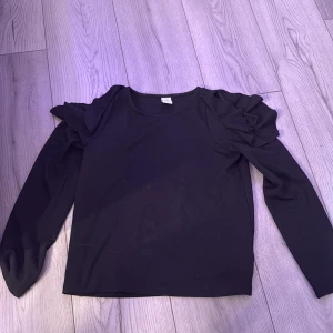 Svart långärmad topp med volang från Lindex - Säljer denna fina tröja från Lindex. Denna tröja har volanger med hål på axlarna. Tjock material inte riktigt som en vanlig långärmad tröja! Köpt för 200kr💞