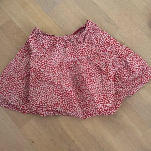 Röd blommig kjol - Supersöt röd kjol med vitt blommigt mönster. Kjolen har en luftig och lätt form, perfekt för varma dagar. Resår i midjan för extra komfort. Passar dig som gillar färgglada och lekfulla plagg!