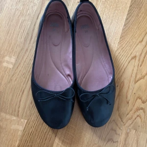 Svarta ballerinaskor - Säljer ett par klassiska svarta ballerinaskor med liten rosett framtill. Skorna har rund tå och en tunn, platt sula. Har små skråmor på insidorna, se sista bilder. Annars bra skick!⭐️ Använda några gånger