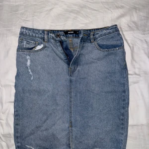 Jeanskjol från BikBok - Säljer en klassisk blå jeanskjol från BikBok i storlek 38. Kjolen har femficksdesign, slitna detaljer och normal passform. Perfekt att matcha med en enkel topp eller hoodie.