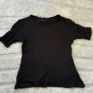 Svart ribbad t-shirt - En enkel svart ribbad t-shirt med korta ärmar och rund halsringning. Perfekt basplagg som passar till det mesta och är lätt att matcha med andra plagg.