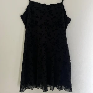 Svart blommig klänning med tunna axelband - Säljer en svart klänning med tunna axelband och blommigt mönster. Klänningen har en lätt genomskinlig mesh med blommor och ett tunt svart tyg under. 💕