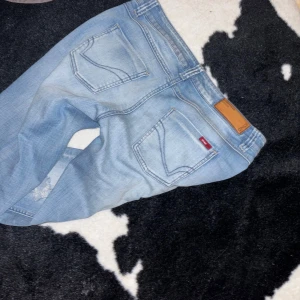 Ljusblå slitna jeans från ONLY - Säljer ett par ljusblå jeans från ONLY med slitna detaljer på benen och klassisk femficksdesign. Jeansen har normal passform och dragkedja i gylfen. Perfekta för en avslappnad stil.