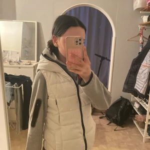 Vit dunväst med huva från Zara - Säljer en vit dunväst från Zara med huva och dragkedja. samt ett röd- och svart-rutigt foder.  snygg till många outfits.