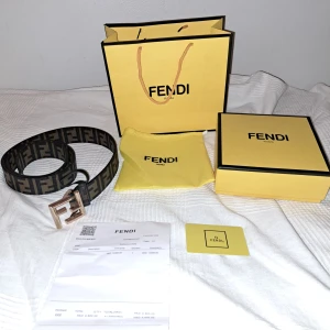 Fendi bälte - TAR EMOT BYTEN‼️Säljer ett Fendi bälte med klassiskt FF-mönster i svart och brun.. Bältet har ett stort metallspänne i form av Fendi-loggan och är gjort i canvas med skinn-detaljer. Perfekt accessoar för att lyfta din outfit.