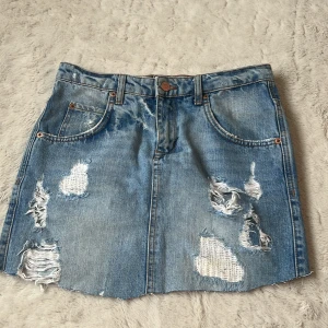 Blå jeanskjol från Perfect Jeans - Säljer en blå jeanskjol från ginatricot  med slitna detaljer och råa kanter. Kjolen har klassisk femficksdesign och knappstängning framtill. De är ett par omklippta jeans💞