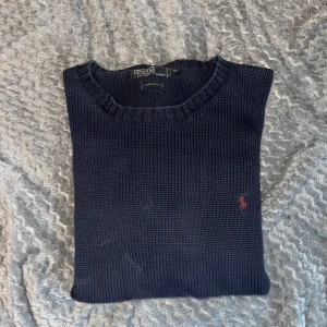  Stickad tröja från Polo Ralph Lauren - Klassisk mörkblå stickad tröja från Polo Ralph Lauren i 100% bomull. Tröjan har rund halsringning och en liten röd broderad logga på bröstet. Perfekt för lager-på-lager och enkel att matcha med olika outfits.