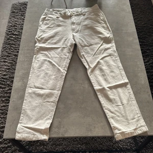 Beige byxor från Jack & Jones - Snygga beige chinos/linnebyxor från Jack & Jones med rak passform och klassisk design. Byxorna har fickor både fram och bak samt stängs med knapp och dragkedja. Perfekta för en stilren och avslappnad look. Storlek 29W/30L