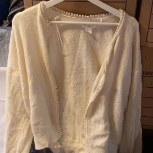 Vit kofta med pärldetaljer från Lindex - Superfin vit kofta med pärlor längs kanterna och runt halsen. Mjuk och fluffig känsla, perfekt att slänga på sig över en topp. Långärmad och öppen framtill, ger en lyxig och söt look.