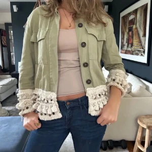 Grön zara jacka med virkade detaljer och tofsar - Snygg och trendig ljusgrön jacka med stora knappar och unika virkade spetsdetaljer och tofsar vid ärmsluten. Jackan har två bröstfickor och är midjekort med rak passform. Perfekt för dig som vill sticka ut med en bohemisk touch. Jackan har två mindre röda färgfläckar på framsidan men inget som märks överhuvudtaget (går säkert att få bort men har ej försökt)🤩