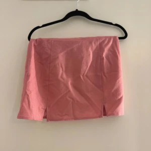 Rosa kortkjol med slits - Säljer en rosa kortkjol i bomull med två små slitsar framtill. Kjolen har en tight passform och är perfekt för dig som gillar en enkel men snygg stil. Passar till många olika toppar och skor.