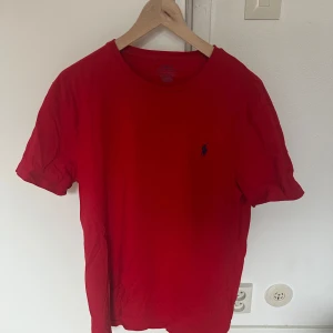 Röd t-shirt från Polo Ralph Lauren - Säljer en röd t-shirt från Polo Ralph Lauren med klassisk passform och liten broderad logga på bröstet. T-shirten är i bomull och har korta ärmar. Perfekt för dig som gillar stilrena basplagg.
