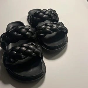 Svarta sandaler med flätade remmar från Duffy - Säljer ett par svarta sandaler från Duffy med två breda, flätade remmar över foten. Skorna har platt sula och är tillverkade i syntetmaterial. Perfekta för varma dagar och ger en trendig look till din outfit. Skriv bara om du har en fråga, priset kan diskuteras!