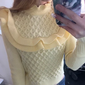 Gul stickad tröja med volangdetaljer - Säljer en söt gul stickad tröja med volangdetaljer runt halsen. Tröjan har ett fint mönster och långa ärmar, perfekt för att lysa upp garderoben. Passar bra till både jeans och kjol. 🌼