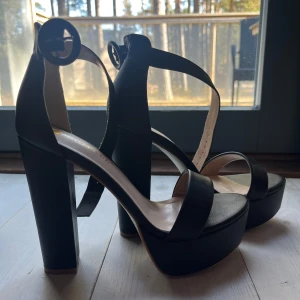 Svarta högklackade sandaler från Bigtree - Snygga svarta sandaler med hög klack och platåsula från Bigtree. De har en justerbar rem med rund spänne runt ankeln för en säker passform. Gjorde själv extra hål i remmet. Heel to toe: 23,5 cm. 