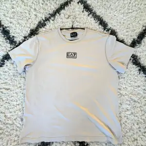 Säljer en stilren beige t-shirt från EA7 med logga på bröstet. Perfekt för en avslappnad look. Passar bra till både jeans och shorts.