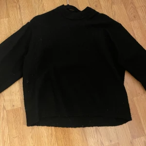 Svart tröja från H&M - Säljer en klassisk svart stickad tröja från H&M. Perfekt för kyligare dagar med sin enkla design och bekväma passform. Tröjan har långa ärmar och en rund halsringning.