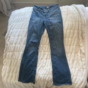 Blå jeans från Nelly - Snygga blå jeans från Nelly med bootcut-stil. De har en låg midja. Bakfickorna har dekorativa knappar. Använda mycket men väldigt bra skick