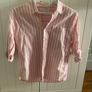 Rosa och vit randig skjorta från Zapa - Säljer en stilren rosa och vit randig skjorta från Zara. Skjortan har långa ärmar som kan rullas upp och knäppas fast. Perfekt för en avslappnad men ändå snygg look. Tillverkad i ett lätt och bekvämt material.