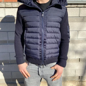 Moncler cardigan - Snygg mörkblå jacka från Moncler med quiltad framsida och stickade ärmar. Jackan har en dragkedja framtill och en huva för extra skydd. Perfekt för kyligare dagar med sin stilrena design. Om ni är intresserade så skriv innnan ni köper! 