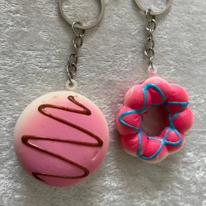 Söta nyckelringar med bakverkstema - Fyra olika nyckelringar med roliga och färgglada bakverksmotiv. Inkluderar en rosa macaron, en rosa munk med blå glasyr, en brödskiva med chokladmönster och en blå kattfigur. Perfekta som accessoarer eller presenter!  45kr/2st/bild , helt ny 