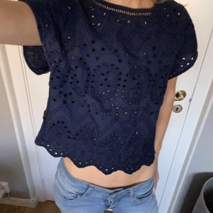 Mörkblå spetsblus  - Säljer en mörkblå blus med vackra spetsdetaljer och korta ärmar. Blusen har ett genombrutet mönster och en croppad passform som ger en trendig look. Perfekt för sommarens varma dagar! Passar xs-s
