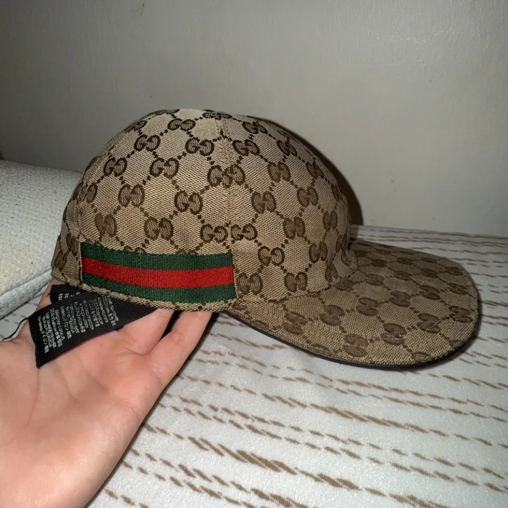 Snygg beige keps från Gucci med det ikoniska monogrammönstret. Kepsen har en justerbar rem baktill och detaljer i grönt och rött på sidan. Perfekt för att ge din outfit en lyxig touch. dustbag finns !. Asusteet.
