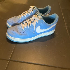 Blå Nike Air Force sneakers - Snygga blå Nike Air Force sneakers med vit sula och vit swoosh. Skorna har klassisk snörning och perforeringar på tån för extra ventilation. Perfekta för en casual look.