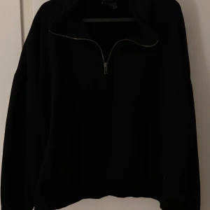 Svart tröja med dragkedja från Monki - Säljer en svart tröja från Monki med dragkedja vid halsen. Perfekt för en stilren och bekväm look. Tröjan har långa ärmar och en hög krage som kan justeras med dragkedjan.