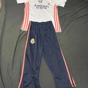 Träningkläder för barn  - Säljer en vit Real Madrid fotbollströja med korta ärmar och tryck på framsidan och baksidan.  Perfekt för fotbollsfans!   Passar nog en som är 9-10 år shortsen är 2/3  #barnkläder #träningskläder
