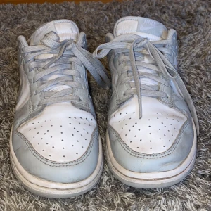 Nike dunk low fog grey - Säljer ett par Nike sneakers i vitt och ljusgrått. Skorna har klassisk snörning och perforerade detaljer på tån för extra ventilation. Perfekta för en avslappnad stil. Nypris 1550 