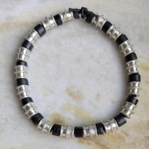 Svart och silver färgat armband - Snyggt armband med växlande svarta och silverfärgade pärlor. Perfekt för att ge en stilren touch till din outfit. Armbandet har en enkel knytning som gör det lätt att justera.