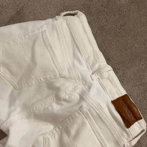 Vita jeansbyxor - Snygga vita jeansbyxor med klassisk femficksdesign och en läderpatch vid midjan. Perfekta för en stilren look.