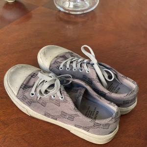 Grå sneakers från Balenciaga - Snygga grå sneakers från Balenciaga med ett diskret mönster och klassisk snörning. Skorna har en vit sula och Balenciaga-loggan på sidan. Perfekta för en stilren look. Box tillbommer, köpta för 7000kr på nk. De ska vara ”slitna” från början kan skicka original bild. Sparsamt använda.