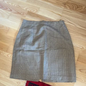 Rutig kjol i beige och svart - Snygg rutig kjol i beige och svart med en klassisk passform. Perfekt för en stilren look. Kjolen är kort och har en normal passning.