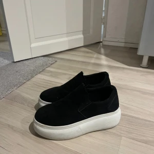 Svarta slip-on sneakers från NLY - Snygga svarta slip-on sneakers med en tjock vit sula. Perfekta för en stilren och bekväm look. Lätta att ta på och av, vilket gör dem praktiska för vardagsbruk. De är lite för stora för mig som har storlek 37 så skulle säga 37,5❤️