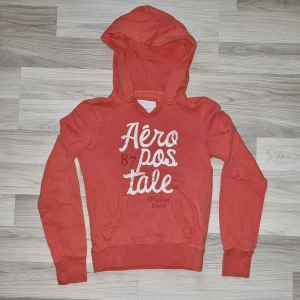 Orange hoodie från Aeropostale - Säljer en snygg orange hoodie från Aeropostale med tryck framtill. Tröjan har en klassisk huva och långa ärmar, perfekt för en avslappnad stil.